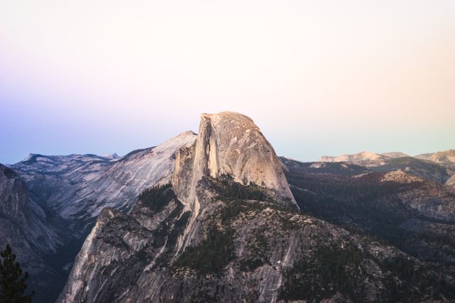 Half Dome in Yosemite National Park is bathed in the soft glow of the setting sun. Perfect for use in travel brochures, websites about national parks, nature calendars, or inspirational posters focused on natural beauty and outdoor adventures.