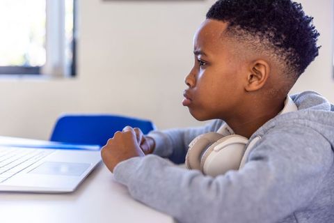 African american boy studying at laptop wearing headphones concentrating on remote learning