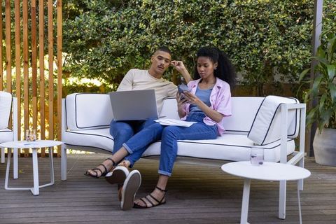 Couple collaborating on budget and remote work on modern patio using laptop and calculator