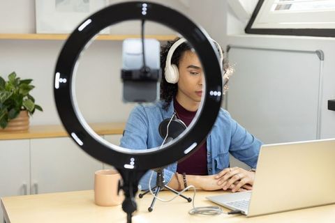 Non-binary creator recording podcast at home using ring light, microphone and laptop