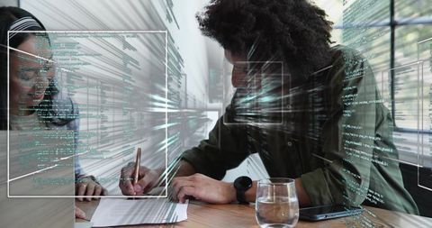 Curly-haired man signing document with teammate in tech workspace with code overlays