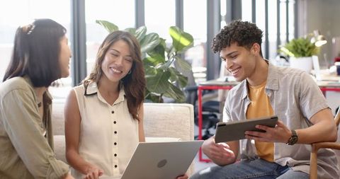 Diverse Coworkers Collaborating on Devices in Modern Office Lounge