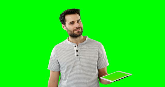 Man holding a tablet with a thoughtful expression on his face. Background features a green screen, ideal for chroma keying to insert any background of choice. Suitable for use in digital content creation, advertising, or technology-related visuals, offering versatility in design.
