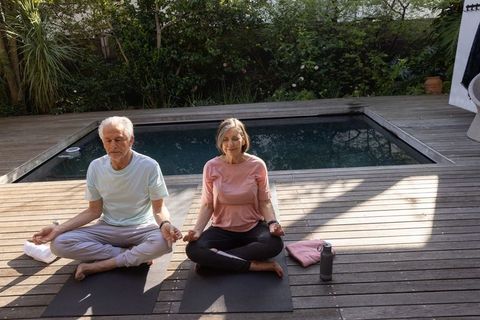 Senior Couple Meditating Outdoors by Pool on Sunny Day