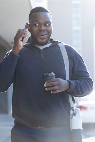 African american man walking, talking on smartphone, holding coffee and shoulder bag