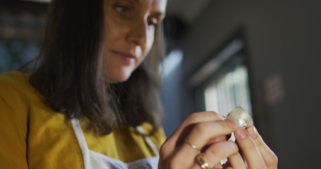 Woman holding and peeling garlic clove, focusing on food preparation. Ideal for healthy eating, homemade cooking concepts, culinary blogs, instructional cooking videos, and kitchen tool advertisements.