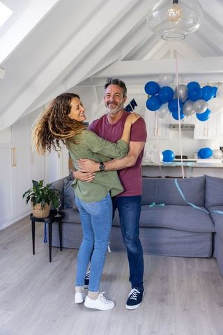 Mature couple celebrating and embracing in bright loft living room with blue balloons