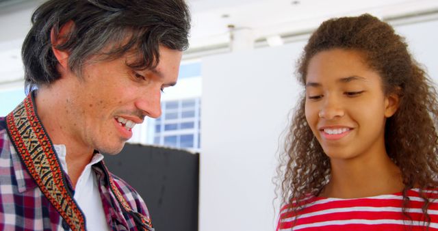 Father and teenage daughter smiling and spending time together. They seem engaged in a bonding activity, possibly chatting or sharing an experience. Nice for use in family-oriented advertisements, parenting blogs, and social campaigns promoting family time and togetherness.