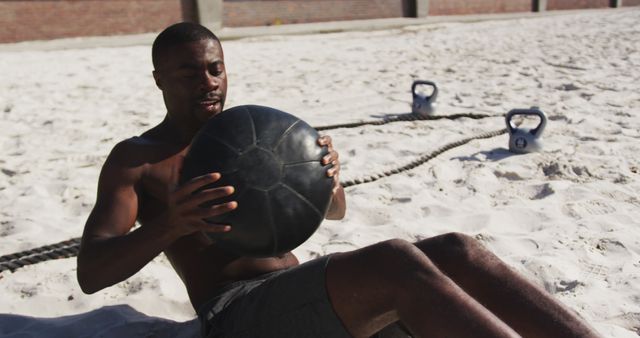Focused african american man doing twists with ball, exercising outdoors on beach. fitness, healthy and active lifestyle concept.