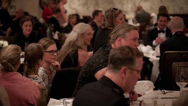 Teen with glasses resting chin on hand at elegant banquet table during formal dinner
