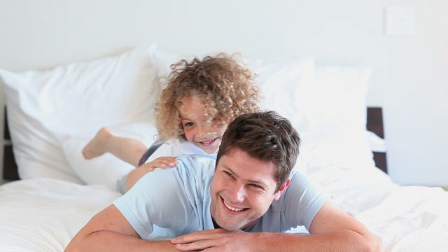 Father and son are enjoying quality time with playful moment on bed, fostering strong family bond. Great for content focused on family life, parenting, joy of childhood, or use in advertisements showing happy home environments.