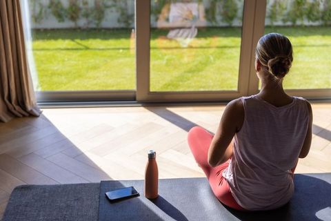 Sunlit home meditation woman meditating on yoga mat by sliding glass doors