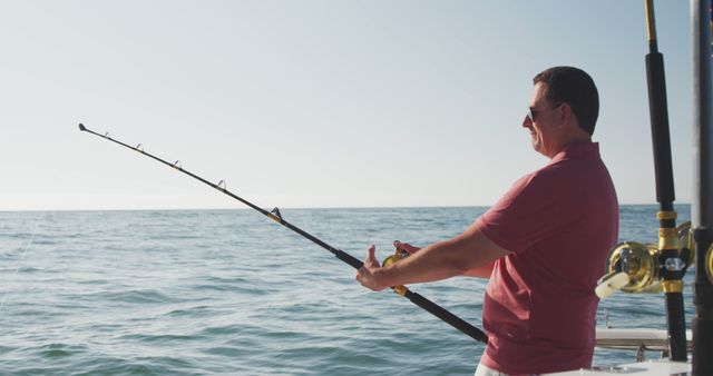 Happy caucasian man in sunglasses fishing from deck of small boat on the ocean on a sunny day. Leisure, hobbies, free time, travel and vacations.