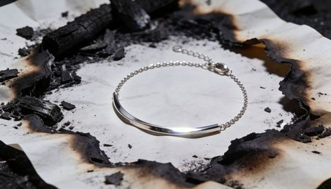 Gleaming minimal silver chain bracelet resting on scorched paper with charred ash