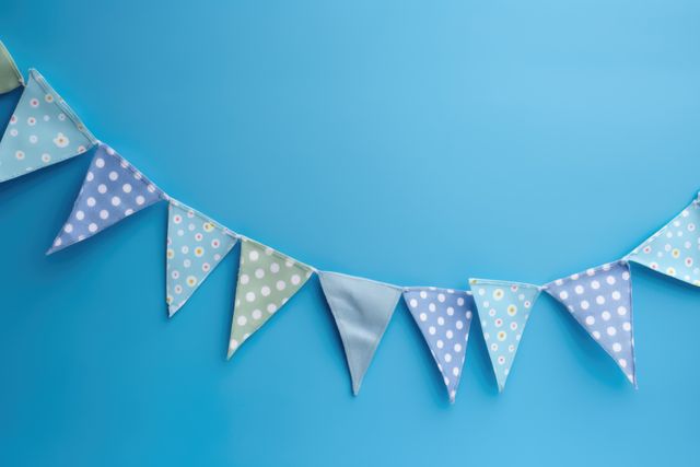 Colorful fabric pennant banner hangs against a blue background with various patterns such as polka dots and solid colors. Ideal for use in festive and party-related settings, particularly for events such as birthday parties, baby showers, or home decor. It conveys a cheerful and celebratory mood in a simplistic design.
