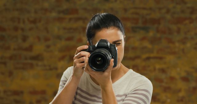 Portrait of caucasian woman taking photo with camera in front of brick wall. Gestures, expressions and virtual reality, unaltered.
