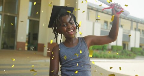 Joyful boy celebrating graduation with diploma amidst gold confetti