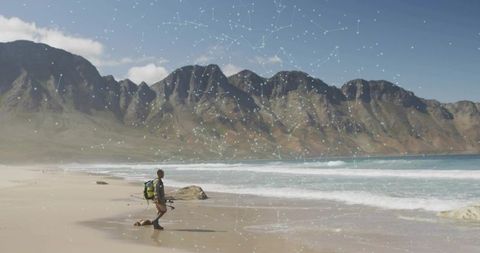Standing angler casting on remote mountain beach wearing waders and green backpack