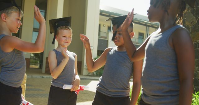 Children in casual attire are seen celebrating their graduation ceremony outdoors. They wear graduation caps and hold diplomas, engaging in friendly, congratulatory gestures. This scene represents academic achievement, teamwork, and the joy of finishing a milestone. Ideal for educational materials, school promotion, and articles on childhood milestones.