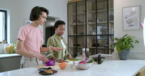 Couple cooking together on marble kitchen island chopping purple cabbage and veggies
