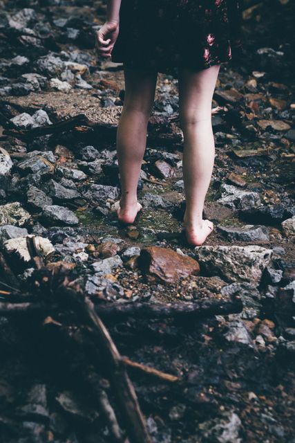 Barefoot person walking on rocky trail in forest, showing legs in dress. Suitable for topics such as nature exploration, outdoor adventure, wilderness therapy, and minimalist lifestyle. Can be used for environmental awareness campaigns, adventure blogs, and promotional material for nature excursions.