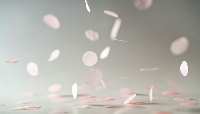 Floating pale pink confetti discs drifting over smooth grey surface minimal still life