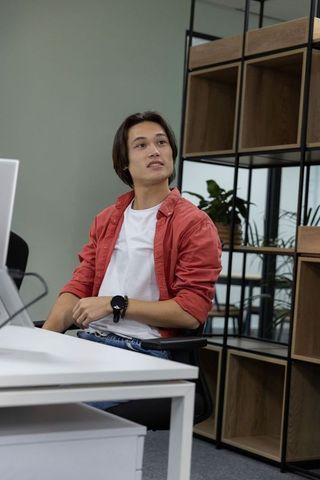 Asian man sitting at desk checking monitor in modern minimalist office with plants