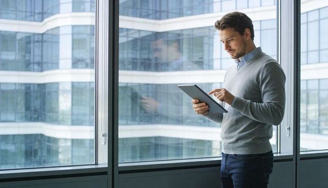 Young professional tapping tablet by office window in modern glass building
