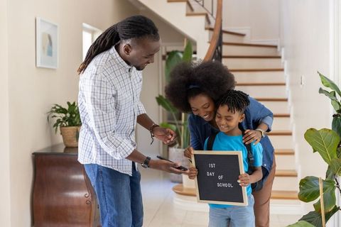 African american parents celebrating child holding 1st day of school letter board at home