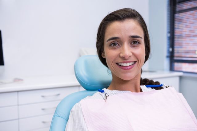 Woman smiling while sitting in a dental clinic chair. Ideal for use in healthcare, dental care, and oral hygiene promotions. Can be used in advertisements for dental clinics, patient care brochures, and healthcare websites.
