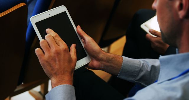 Photo features businessman using a digital tablet during a conference presentation. This image is ideal for depicting business communication, corporate settings, technology in professional environments, and digital interactions during meetings. Useful for websites, articles, and promotional materials focused on business technology, conferencing solutions, and professional networking.