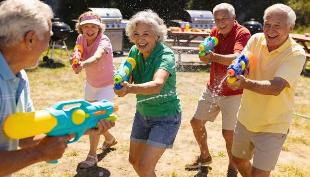 Seniors playing water gun battle in sunny backyard barbecue, laughing together