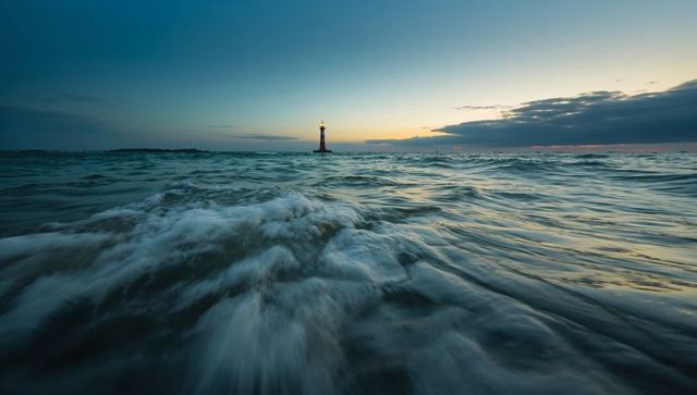 Lighthouse beacon guiding rolling ocean waves at twilight with glowing sunset horizon