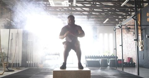 Athletic Man Performing Powerful Box Jump in Fitness Gym