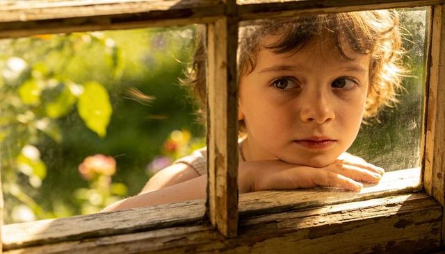 Child gazing through weathered window at sunlit garden, contemplative golden-hour portrait