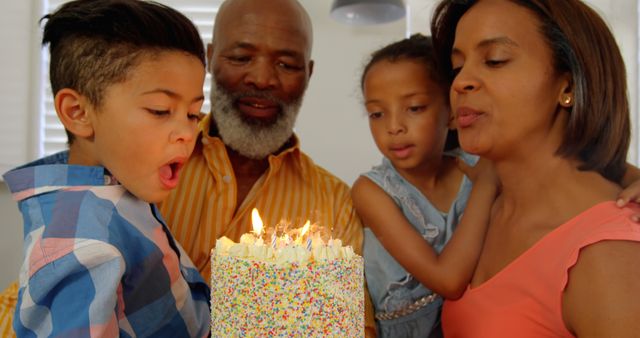 Front view of black family celebrating birthday in kitchen of comfortable home. Boy blowing out candles on a birthday cake 4k