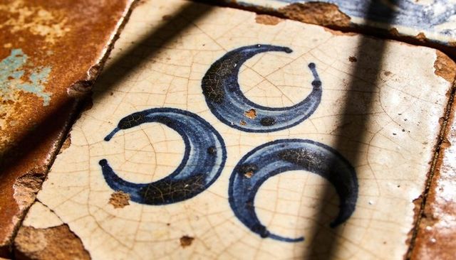 Aged ceramic tile with blue crescent motif and crackle glaze on weathered mosaic surface