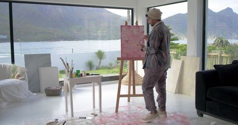 Indian male artist painting pink abstract canvas in sunlit waterfront studio