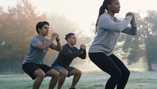 Morning outdoor group workout squats on dewy grass — diverse adults training
