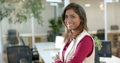 Confident indian businesswoman smiling with arms crossed in modern open-plan office workspace