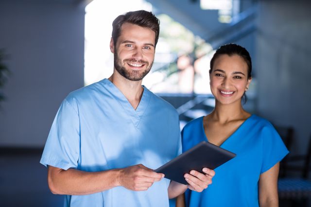 This image shows two smiling medical professionals in a hospital setting, using a digital tablet. Ideal for illustrating modern healthcare, teamwork, and the use of technology in medical environments. Suitable for healthcare websites, medical blogs, and promotional materials for medical technology.
