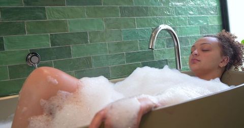 African american woman relaxing in bubble bath with chrome faucet and green tile wall