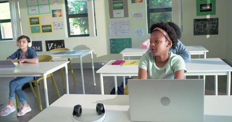 Multicultural students using laptops and headphones in sunlit modern classroom
