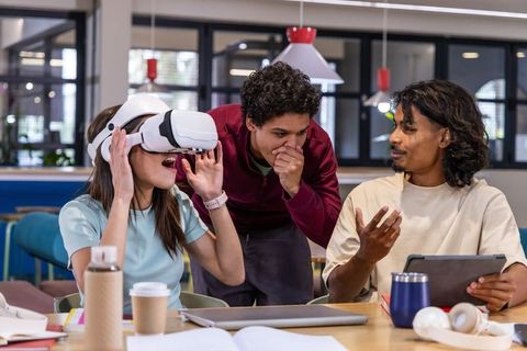 Asian woman experiencing VR headset while diverse team collaborating in modern coworking