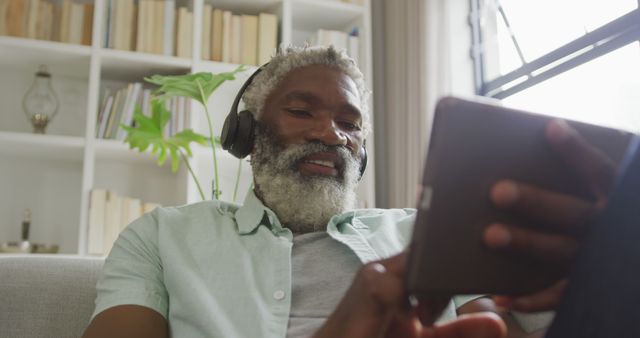 Image of african american senior man using tablet and headphones. retirement lifestyle, spending time alone at home concept digitally generated image.