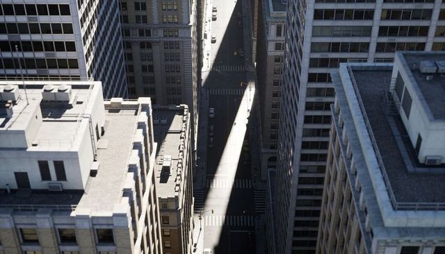 Catching diagonal sunlight cutting through urban canyon from rooftop, aerial downtown street