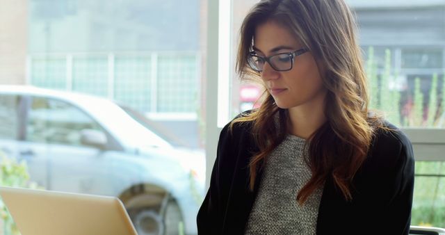 Woman Wearing Glasses Working on Laptop in Urban Office Setting - Download Free Stock Images Pikwizard.com