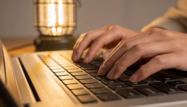 Typing hands on laptop keyboard under warm lamp light for cozy remote work and study
