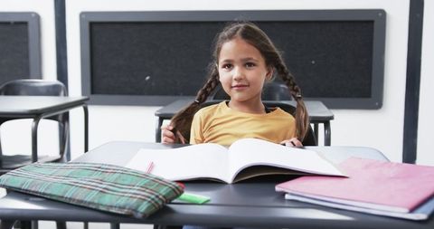 Young Student Sitting at Desk with Books in Classroom