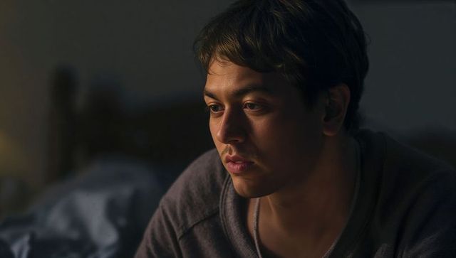 Pensive young man in dim bedroom light, moody intimate portrait with warm tones